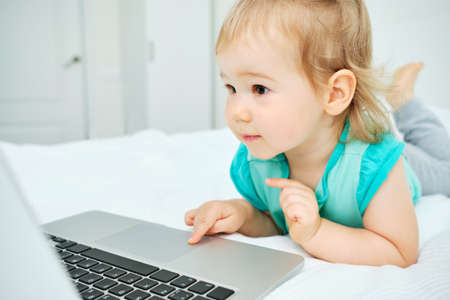 Happy and smiling kid uses her laptop lying on the bedの写真素材
