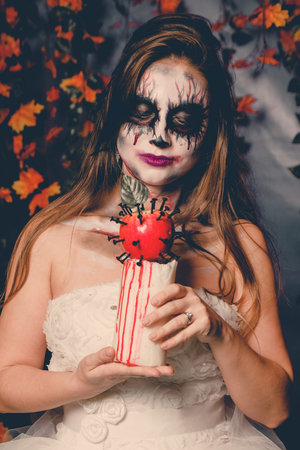 Woman with halloween makeup in wedding dress holds a blood apple.