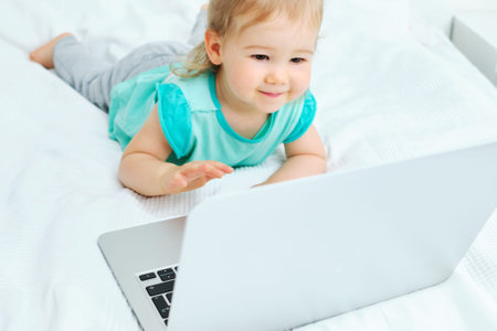 Happy smiling caucasian kid girl clicks on laptop.