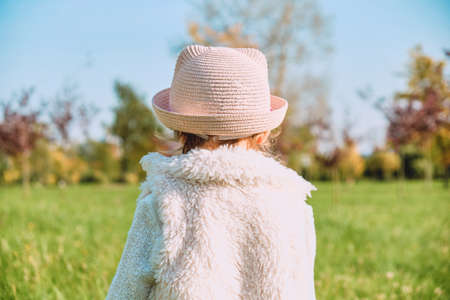 Caucasian child girl in rustic clothes walks with her back in the autumn park.の写真素材