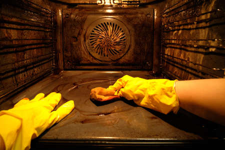 A person in protective gloves washes the dirty oven from traces of food inside with the light on.の写真素材