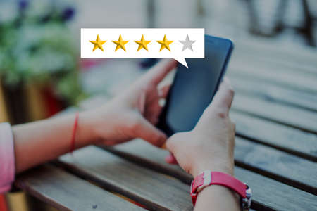 A girl puts a rating from the stars and a review in a smartphone while sitting in a cafe on the street in summerの写真素材