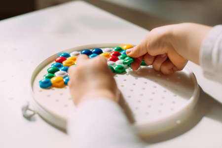 A toddler with both hands lays out a colored mosaic in a plastic mold.の写真素材