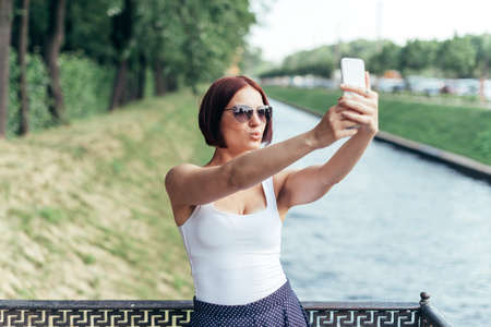 Red-haired girl in sunglasses makes a photo on a smartphone with a kiss.の写真素材