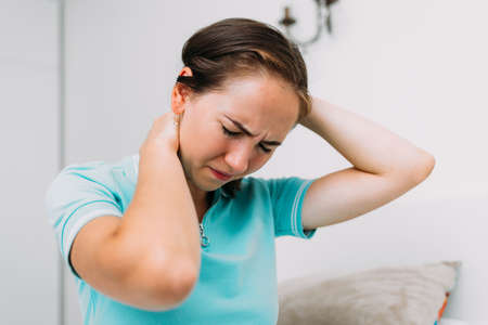 Caucasian woman sitting at home and suffering from pain in the neck and spine.の写真素材