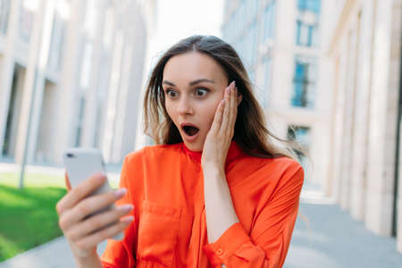 Caucasian woman wonder and shocked looking at a smartphone in her hands.の写真素材