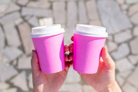The person is holding two pink disposable cups for coffee or teaの写真素材