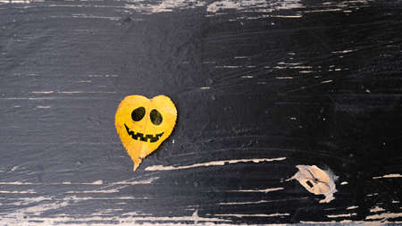 Halloween holiday. Cheerful face painted on an autumn leaf on a wooden background with copy spaceの写真素材