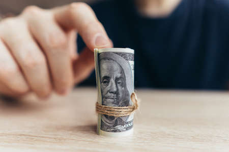 The person points to a rolled stack of dollar bills. The concept of the first earned money.の写真素材