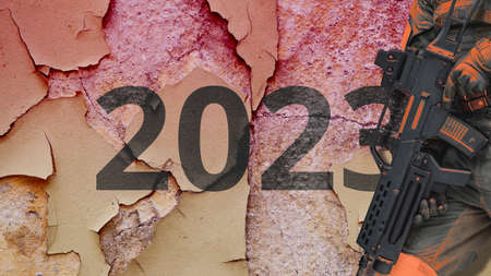 The concept of the new year 2023. A soldier with a machine gun against the background of a broken wallの写真素材
