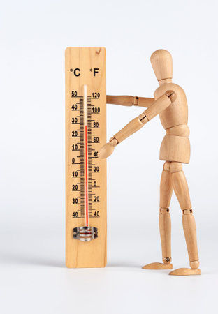 Hot summer weather, a wooden man measures the air temperature: celsius and fahrenheit scale thermometer for measuring air temperature. Objects isolated on white background. 27 Celsius degrees.の写真素材