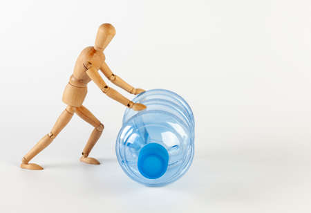 A wooden man rolls an empty five gallon plastic water bottle. Isolated on white on a white background.の写真素材