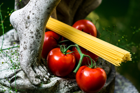 Foot of a statue with tomatoes and spaghettiの写真素材