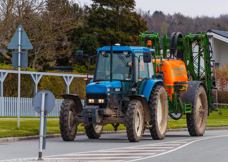 Mogenstrup Denmark - April 29. 2016: Blue tractor with a orange sprayer driving on a road