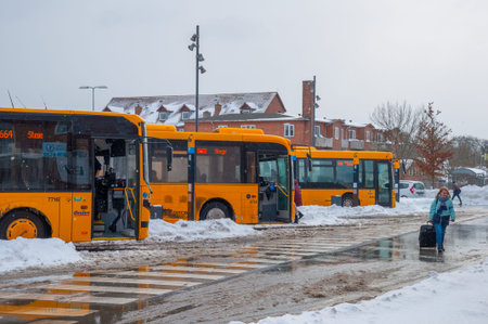 Vordingborg Denmark - February 3. 2018: Buses parked at the bus Terminal on a snowy winter day with a woman pulling her bag on the roadのeditorial素材