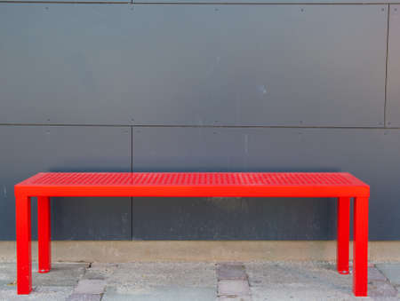 Red bench in front of a grey building facadeの写真素材