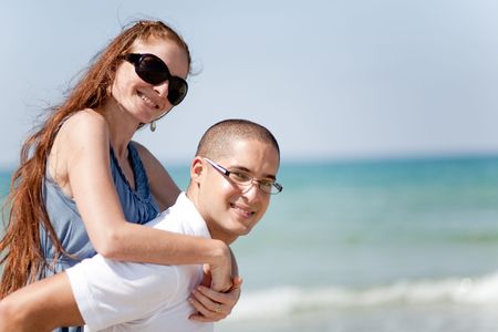 Portrait of Young man piggyback his girlfriend on the beachの写真素材