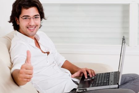 happy young man using laptop showing thumbs up の写真素材