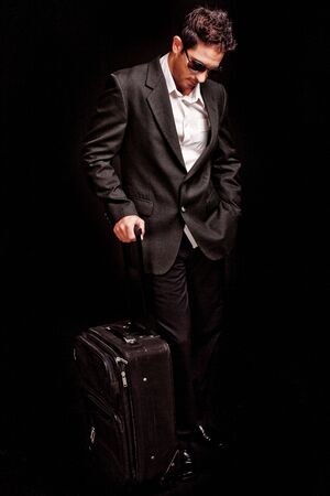 Business man looking down with his luggage on black isolated backgroundの写真素材