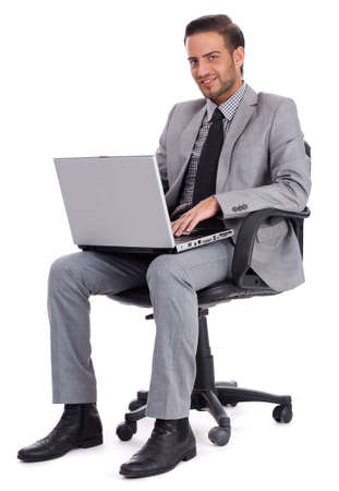 Business man sitting with laptop and smiling at office desk isolated white backgroundの写真素材