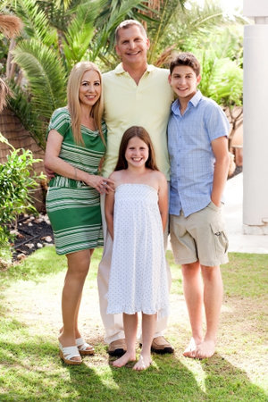 Happy family standing together in their backyard of home looking at you