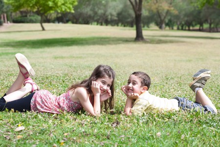 Cute children lie down on green grass and looking eachother in the park, outdoorの写真素材