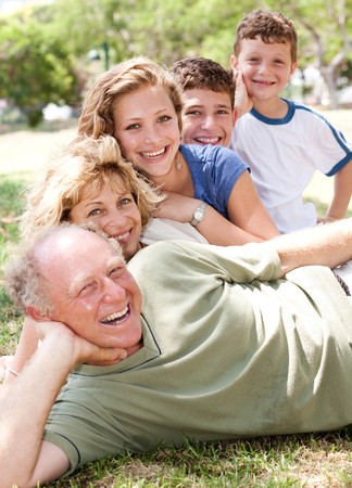 Multi-generation family relaxing in park on sunny day and smiling at cameraの素材 [FY3107448903]