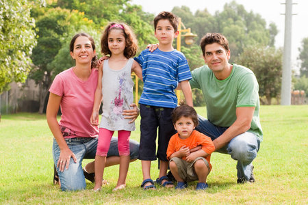 Half seated parents with their children posing to camera in the park on sunny day
