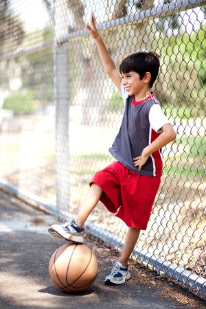 Smiling young boy with his basketball resting against fenceの写真素材