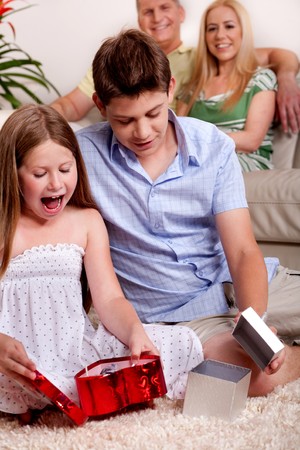 Brother and sister busy in opening christmas gifts with parents in the backgroundの写真素材