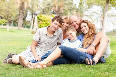 Family of five relaxing on sunny day in the park and smiling at cameraの写真素材