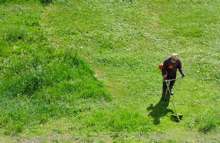 Worker with gas-powered string trimmer beveling green grass