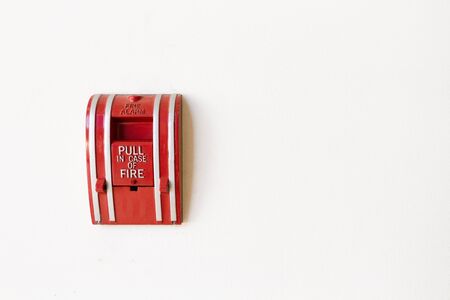 Red fire alarm pull switch on white cement wall