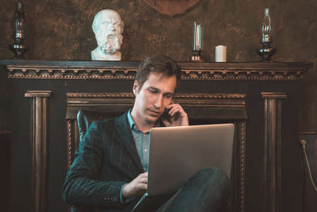 A man is working at a computer and talking on the phone in the background of a fireplaceの写真素材