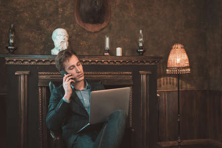 A man is working at a computer and talking on the phone in the background of a fireplaceの写真素材
