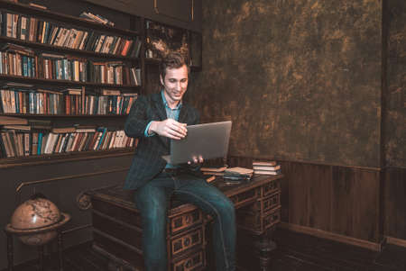 Businessman man sitting on the screech table with a computer on the background of booksの写真素材