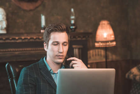 A man talking on the phone and working at the computer on the background of the fireplaceの写真素材