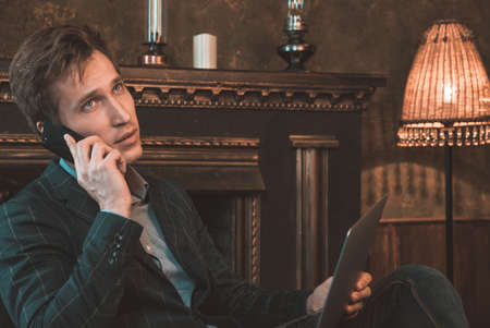 A man talking on the phone and working at the computer on the background of the fireplaceの写真素材