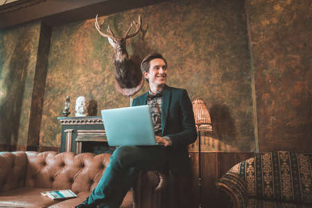 Businessman sitting on the wrinkled leather sofa talking on the phone and typing on the computerの写真素材