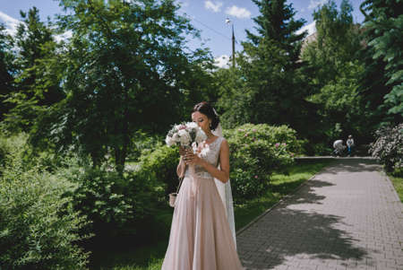 Bride in park with wedding bouquet in hands and beautiful dressの写真素材