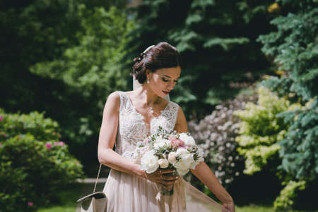 Bride in park with wedding bouquet in hands and beautiful dressの写真素材