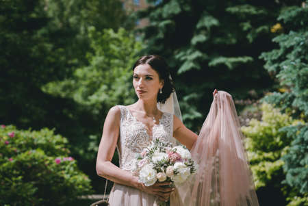 Bride in park with wedding bouquet in hands and beautiful dressの写真素材