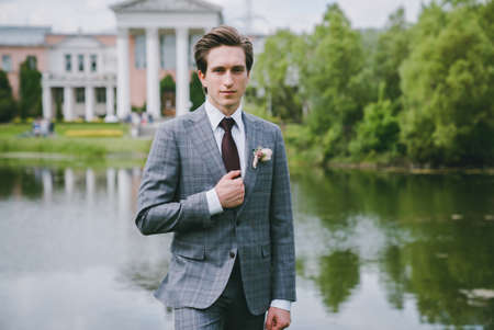 The groom in a suit stands near a lake in the parkの写真素材