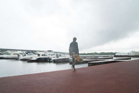 A man is riding a skateboard on a pier in a yacht club near the riverの写真素材