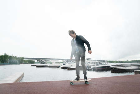 A man is riding a skateboard on a pier in a yacht club near the riverの写真素材