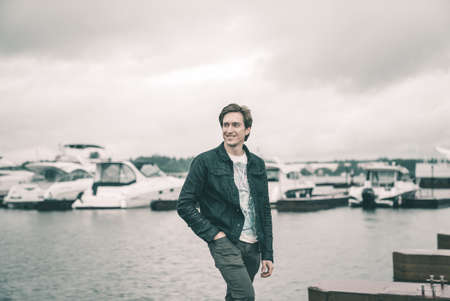 Portrait of a man in a jeans standing on a pier near the yachtの写真素材