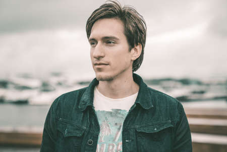 A man in a jeans is standing on a pier in a yacht club near the riverの写真素材