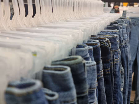 Many jeans hanging on a rack. Row of pants denim jeans hanging in closet. concept of buy , sell , shopping and jeans fashionの写真素材