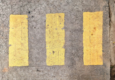 A direct top-down shot of three worn yellow stripes painted on a concrete surface, serving as road markings. This image underscores the necessity of traffic discipline, respecting regulations, and prioritizing safety on the roadの写真素材