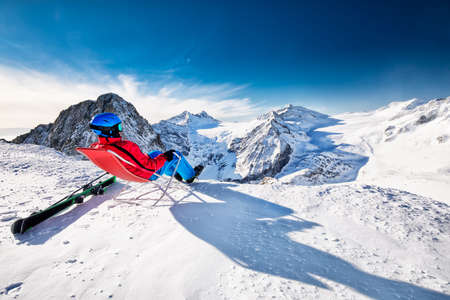 Young happy skier sitting on the top of mountains enjoying the view from Presena Glacier, Tonale, Italyの写真素材